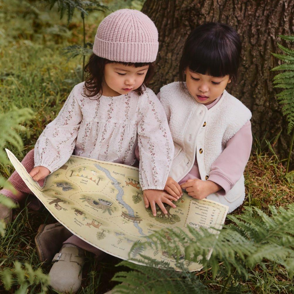 two little girls sitting under a tree looking at a map