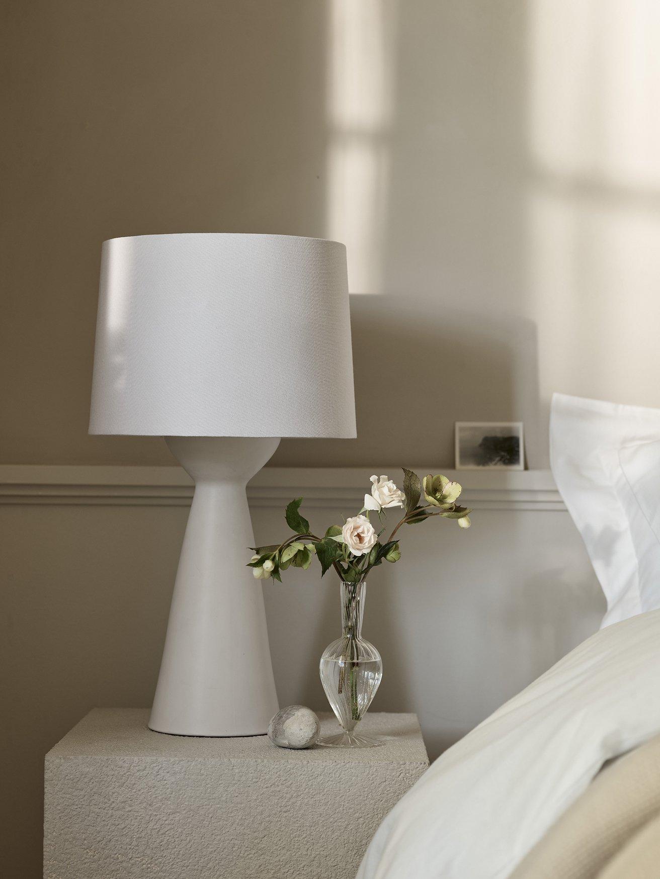 a white bed with a white nightstand and a vase of flowers