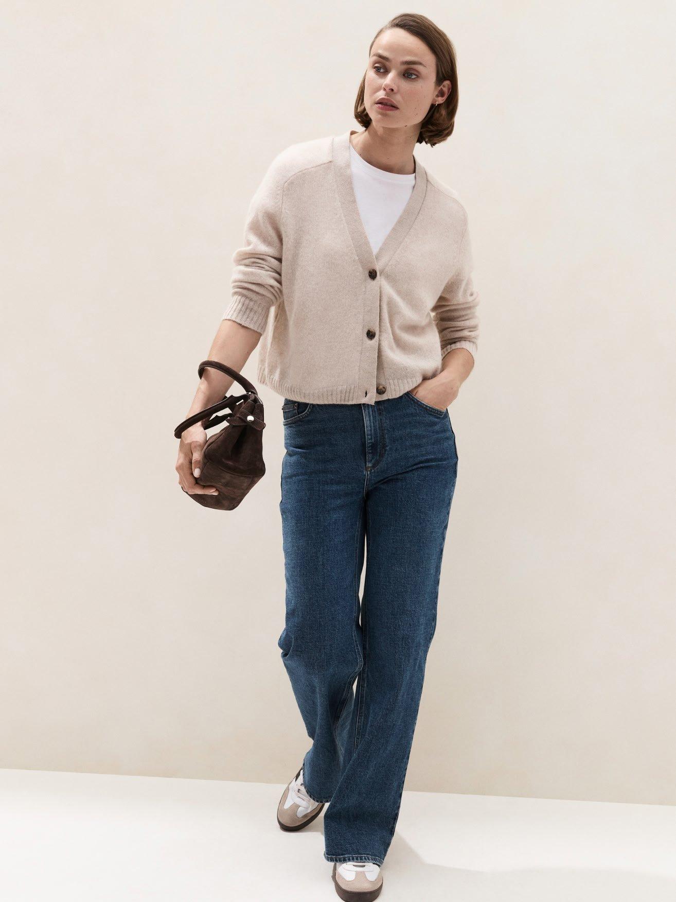 a woman in a cardigan and jeans holding a purse