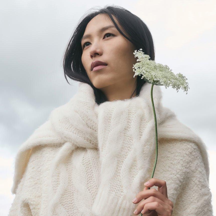 a woman in a white sweater holding a flower in her hand