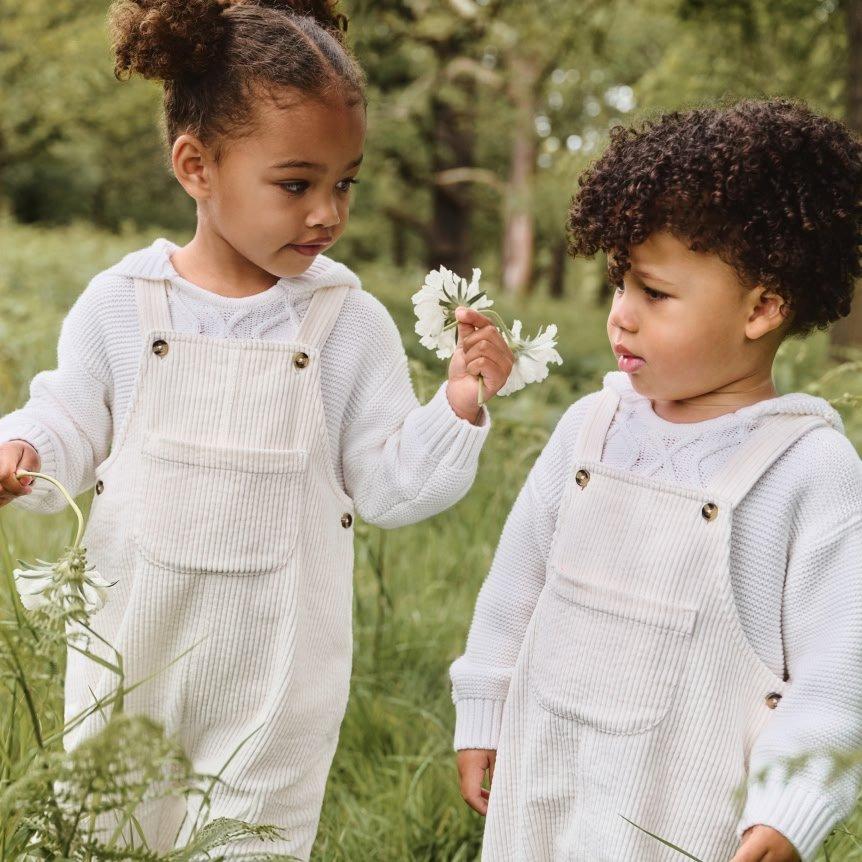 two little girls in overalls standing in a field of grass