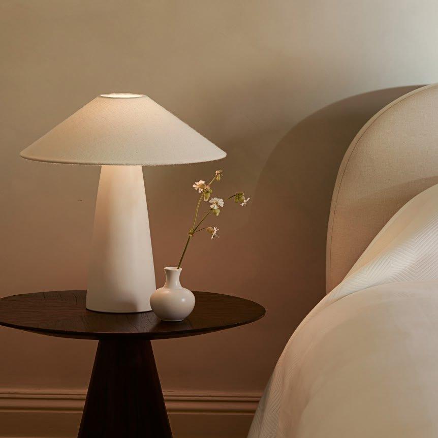 a small table with a vase on it next to a bed