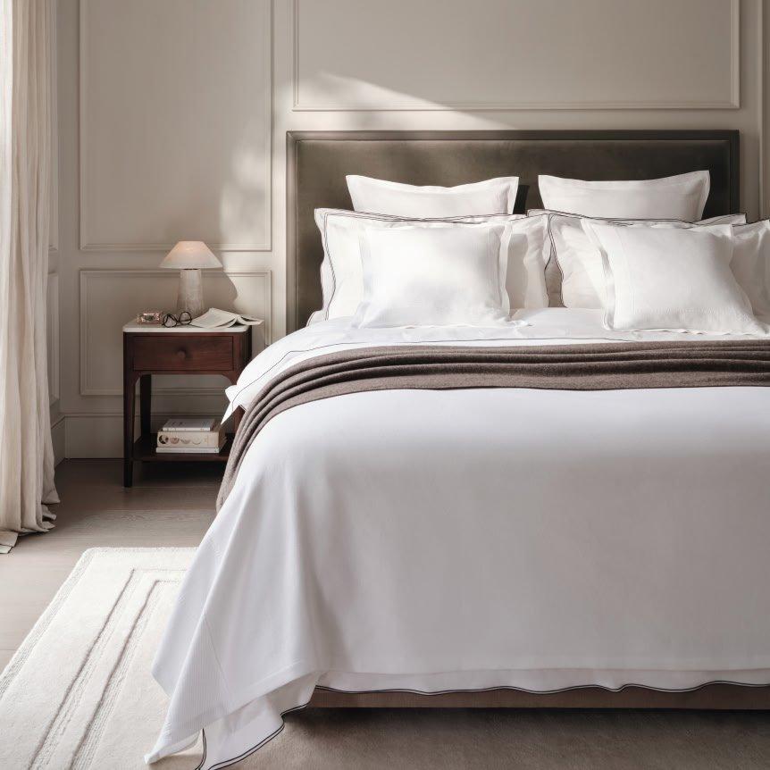 a bed with white sheets and pillows in a bedroom