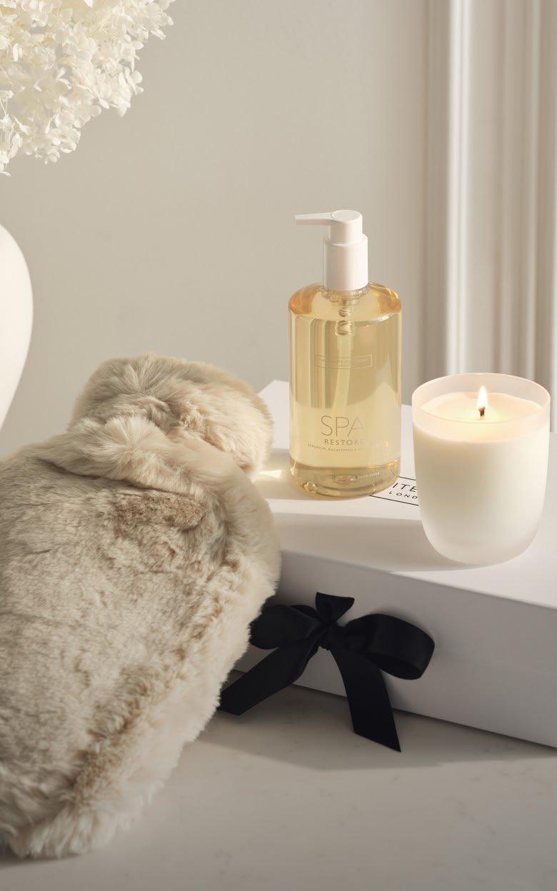 a white candle, a bottle of lotion and a small bottle of perfume