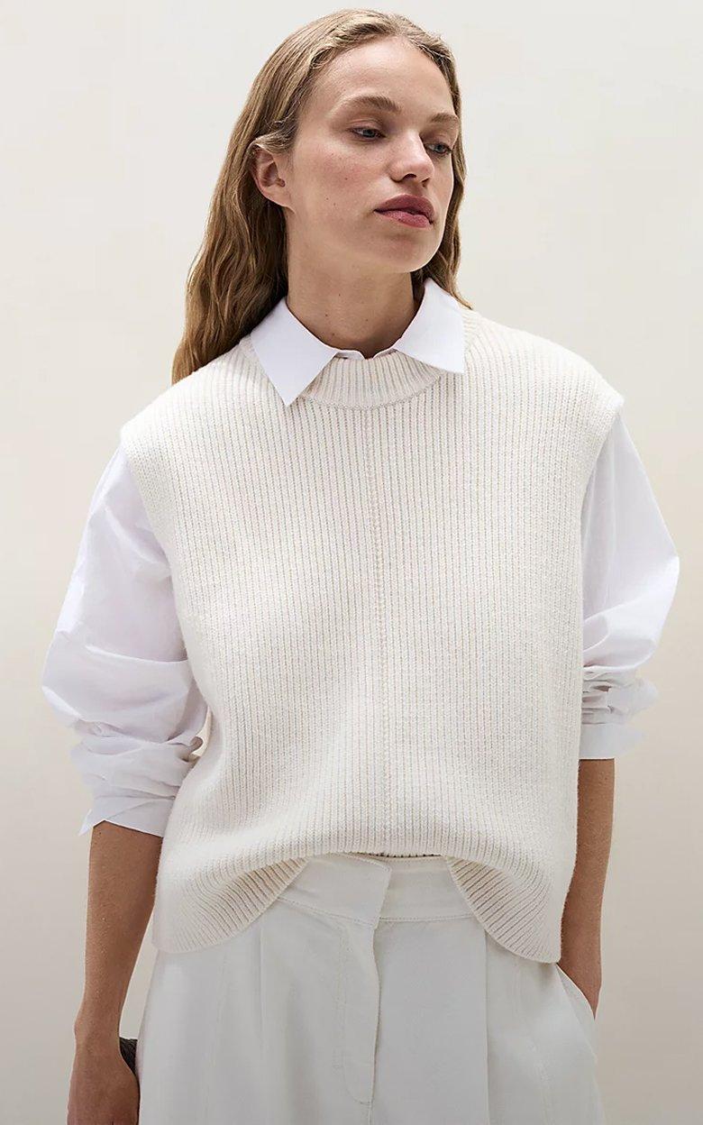a woman in a white sweater and white pants standing up